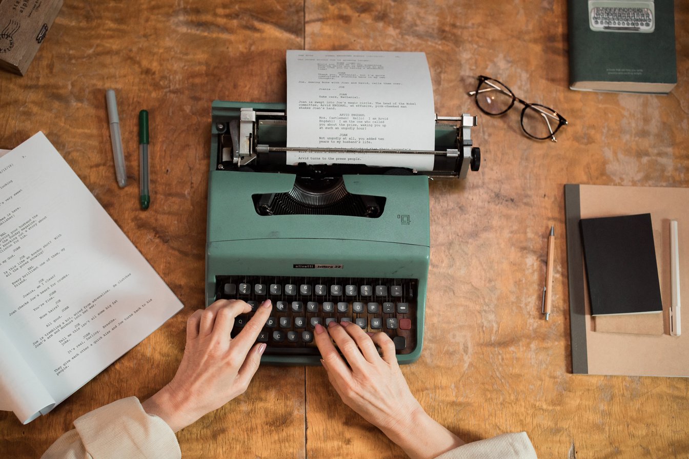 Person Typing on Green Typewriter on Brown Wooden Table